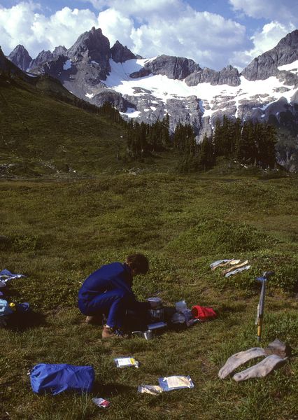 Sue cooking dinner at Yang Yang Lks. / Ptarmigan Traverse / We came through low snow slot to right of image / circa 1985. Photo by Fred Pflughoft.